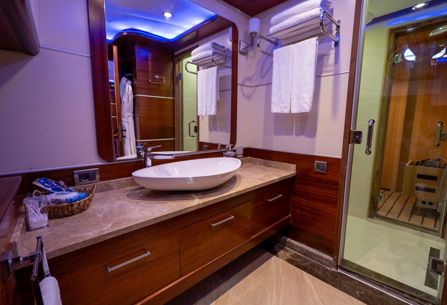 yacht bathroom featuring white vessel sink, marble vanity, wood cabinetry and blue ambient lighting