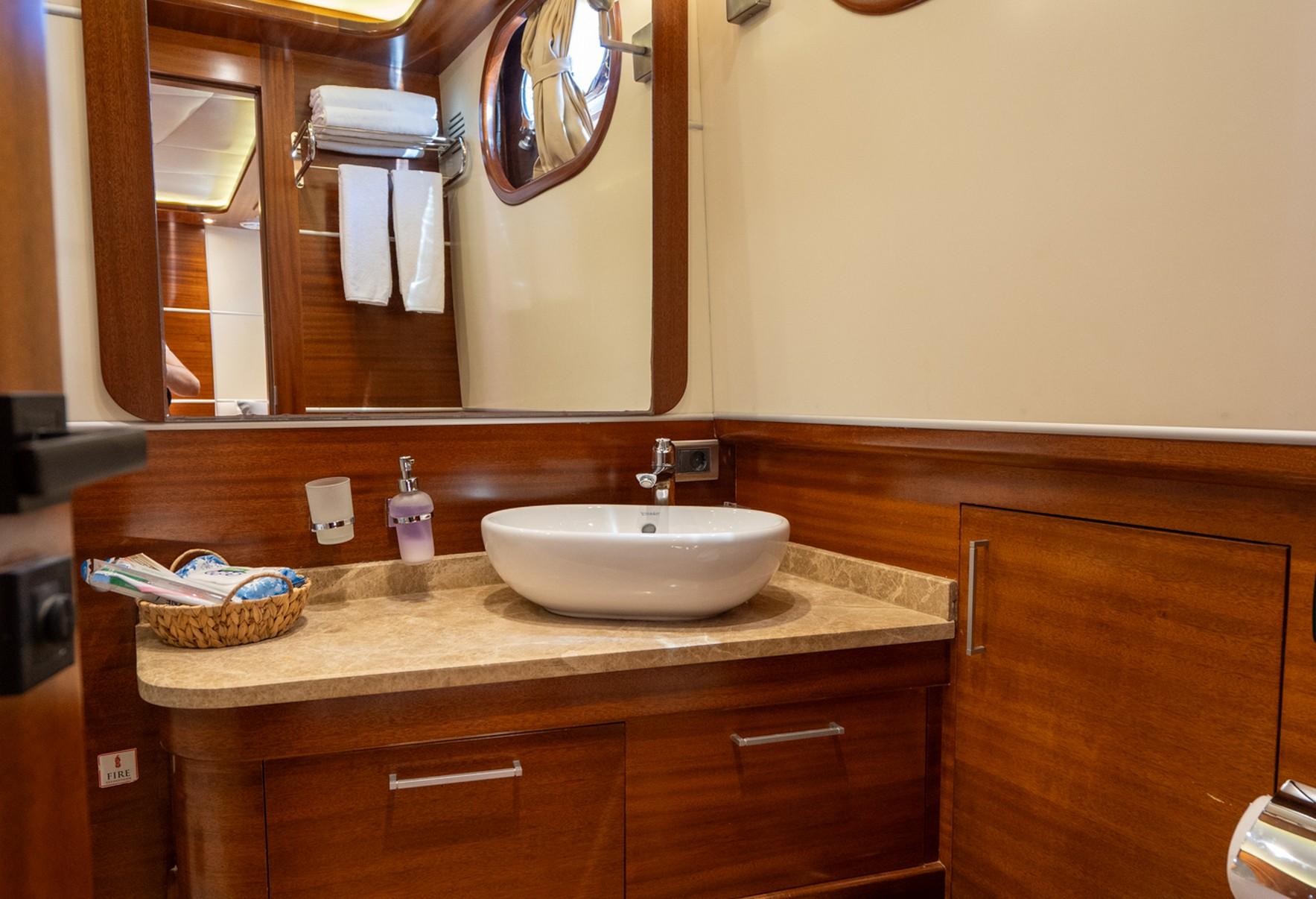 yacht bathroom featuring white oval vessel sink on marble countertop with wood cabinetry