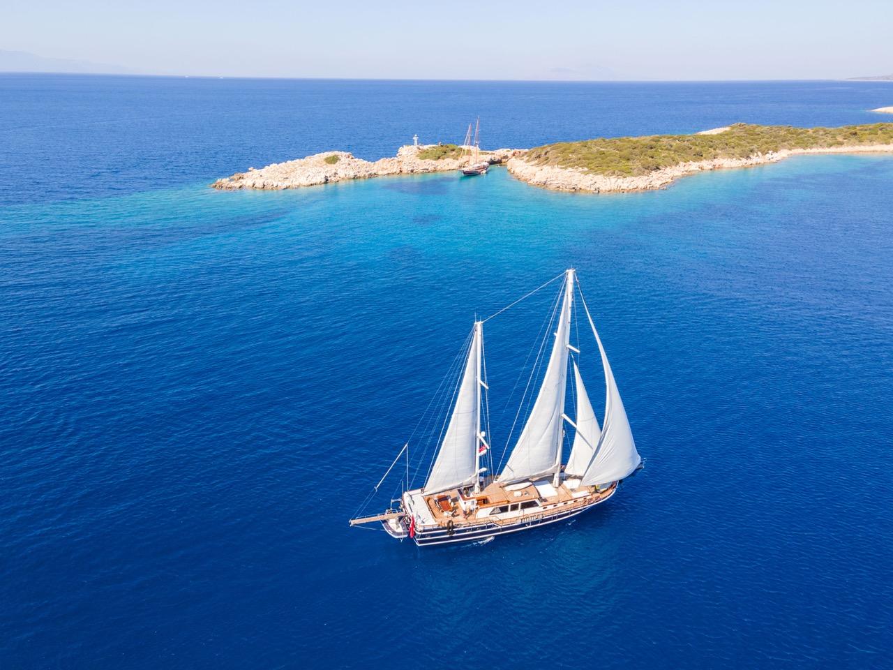 aerial view of traditional white sailing gulet anchored in crystal clear Mediterranean waters near rocky coastline