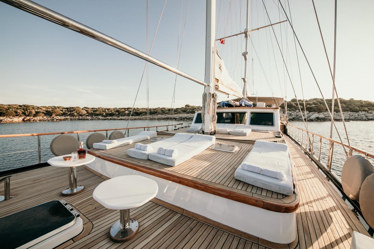gulet foredeck with white cushioned sunbeds and cocktail tables at anchor