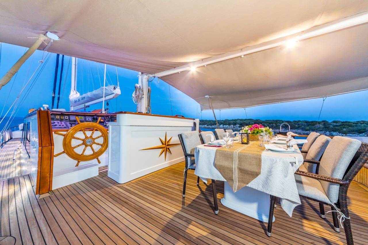 yacht aft deck dining table with white chairs and wooden helm wheel
