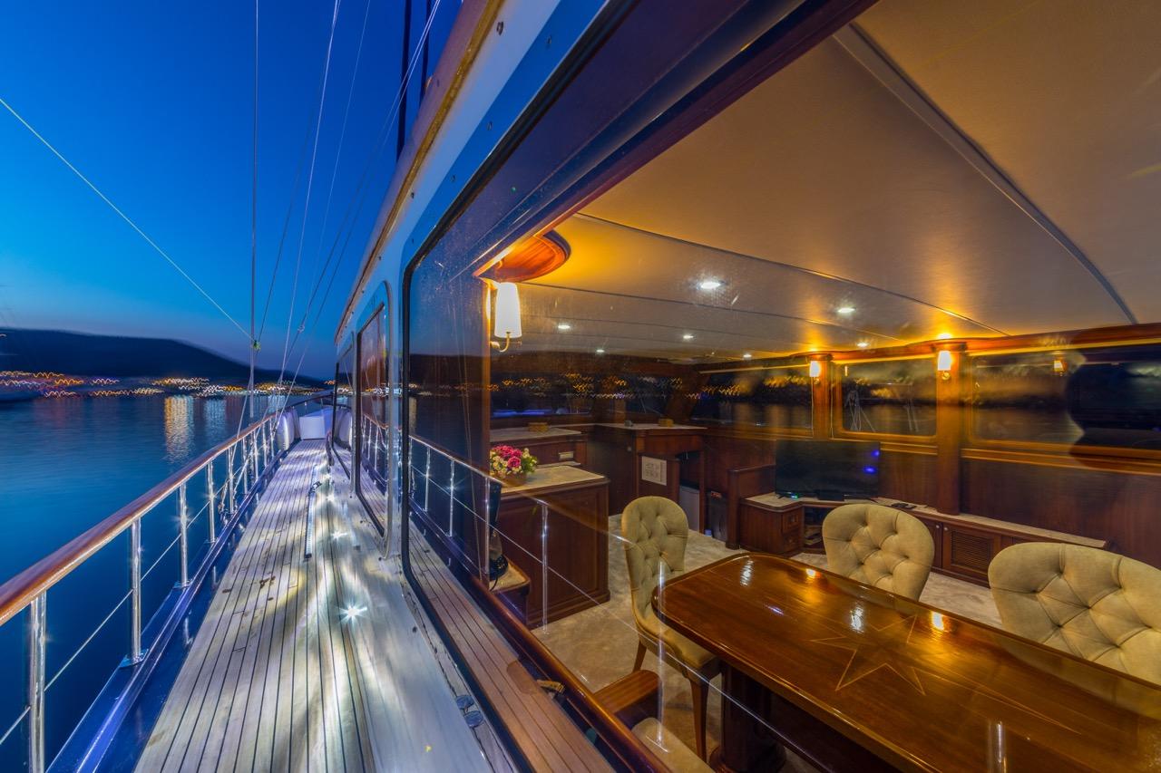 gulet yacht covered aft deck with dining table and cushioned chairs at twilight