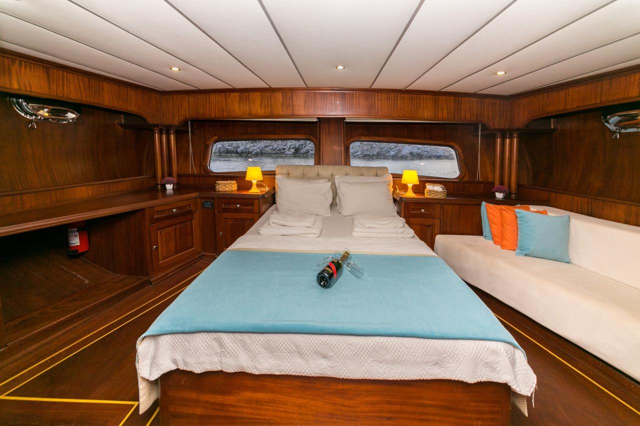 yacht cabin interior with double bed, wooden paneling, bedside tables with yellow lamps and portholes