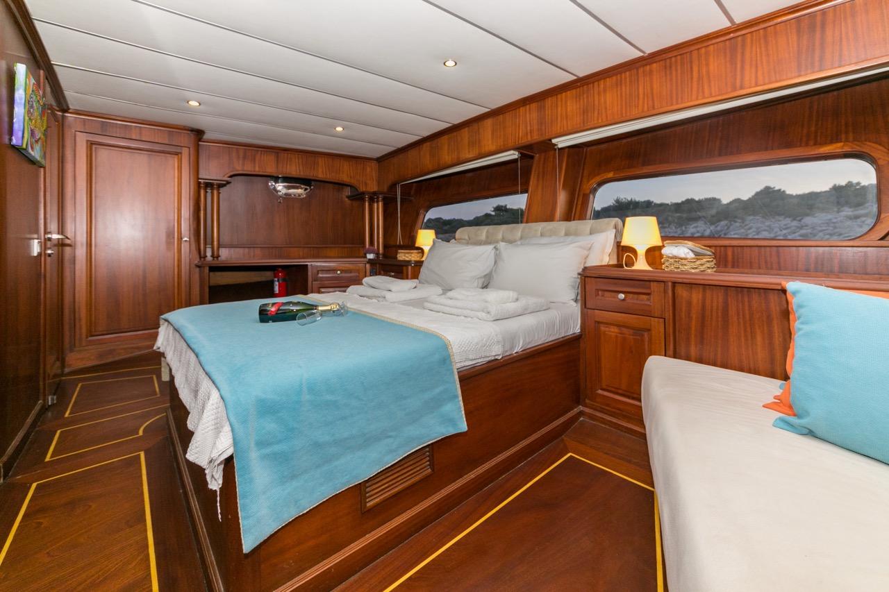 yacht guest cabin featuring double bed with turquoise throw, built-in wardrobes and porthole windows