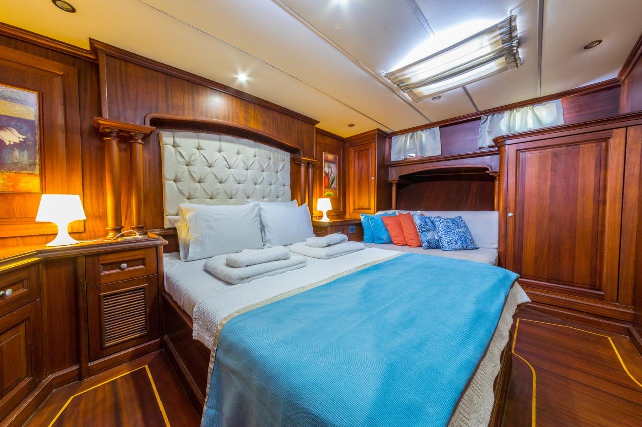 Master cabin interior with white tufted leather headboard, blue bedding, rich wood paneling and built-in storage
