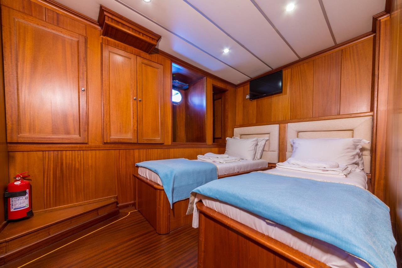 twin cabin with two single beds, white linens, blue throws, and extensive wood cabinetry
