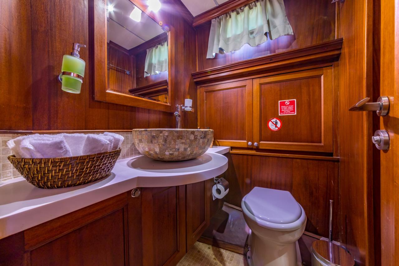 yacht bathroom featuring marble vessel sink, wicker basket, wooden paneling and white toilet