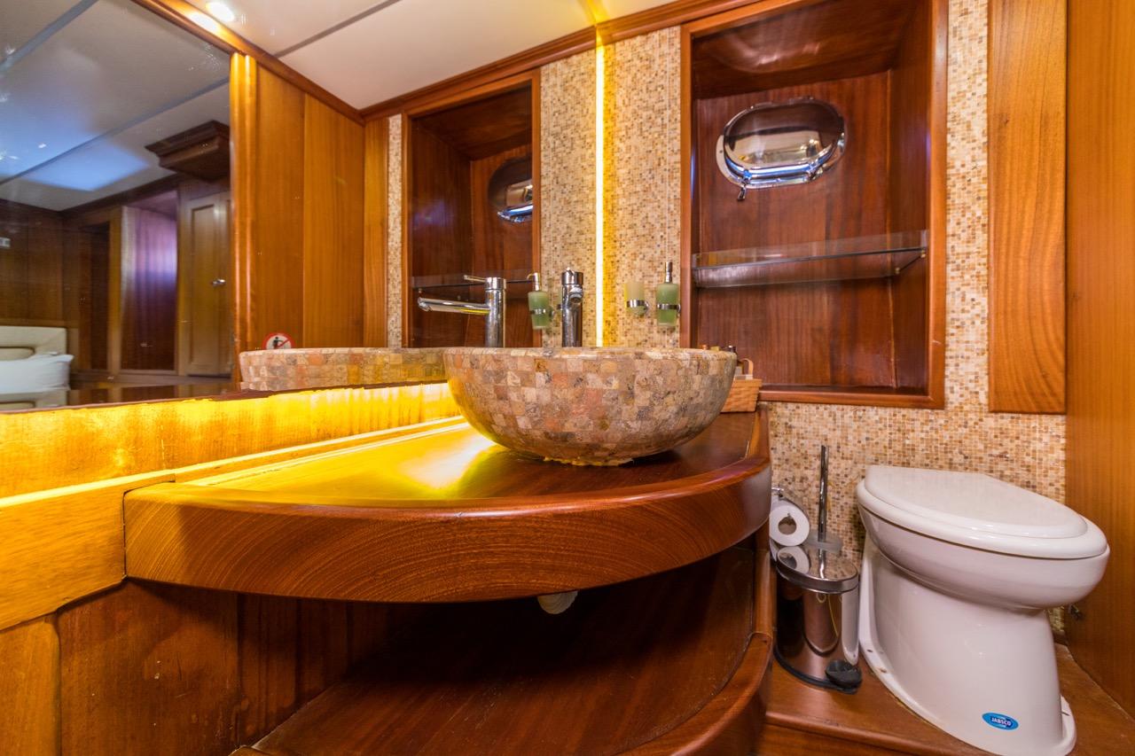 yacht bathroom featuring stone vessel sink, wooden vanity counter, mosaic tile backsplash and toilet