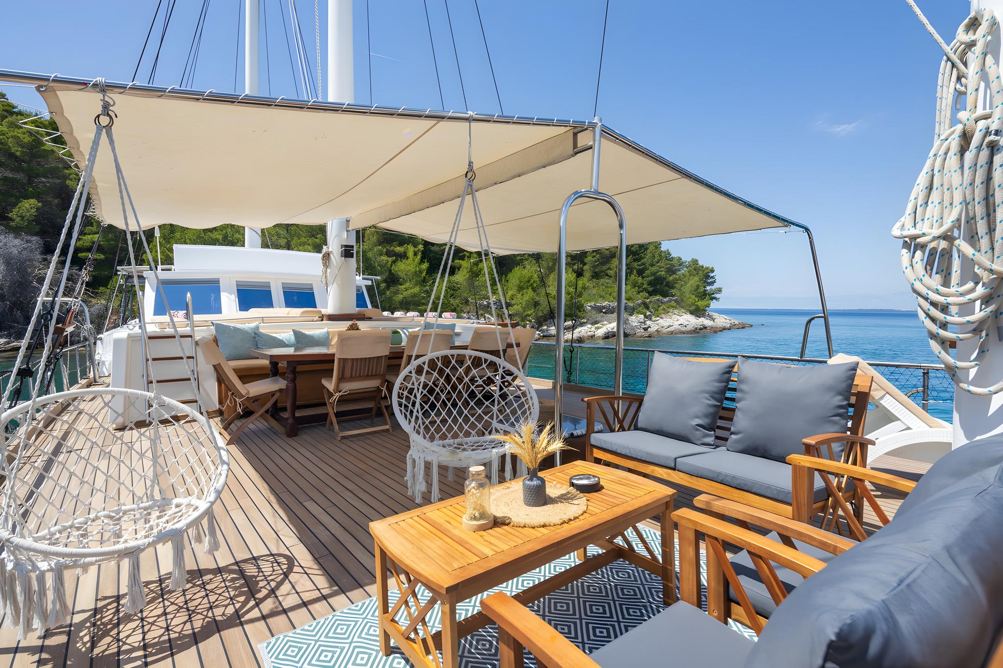 Yacht main deck with covered seating area and hanging chair in Mediterranean bay