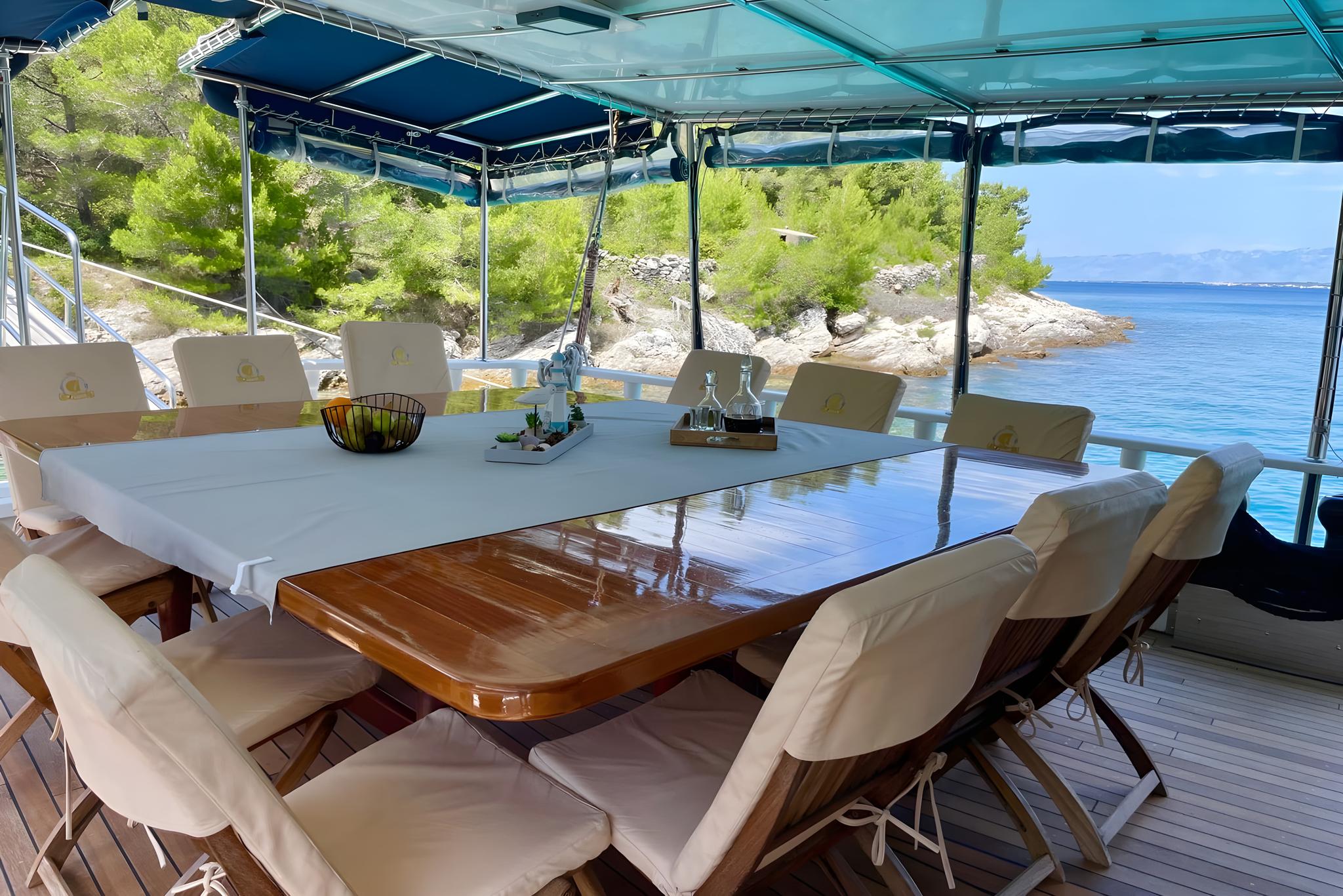 luxury yacht aft deck dining area with wooden table and coastal view