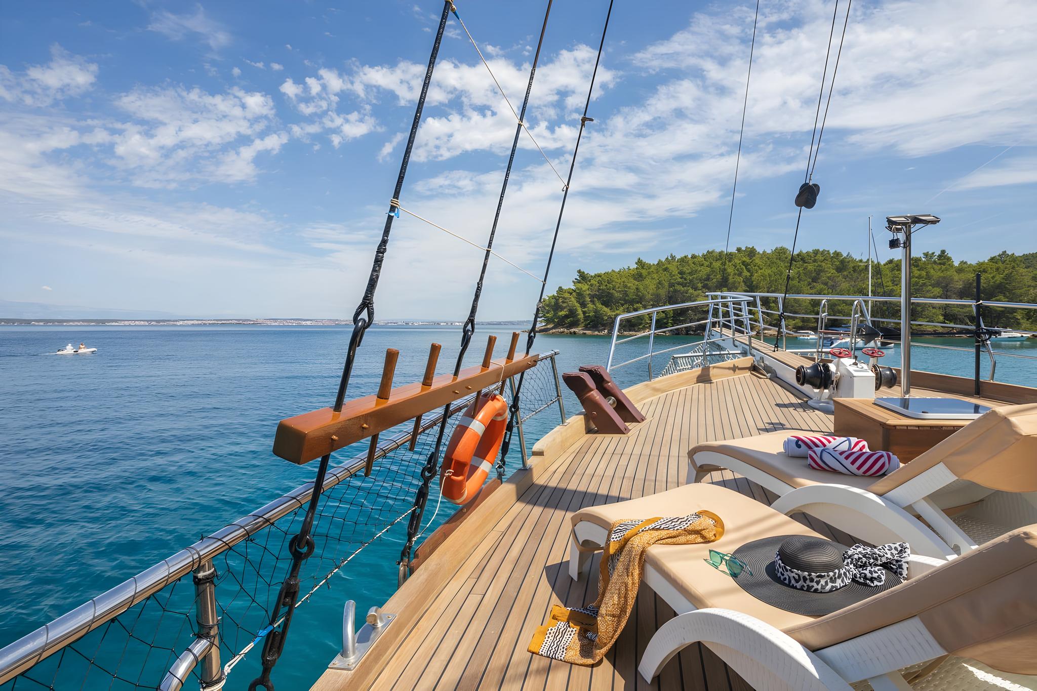 Yacht foredeck with teak decking, sun loungers, and sailing rigging in turquoise waters