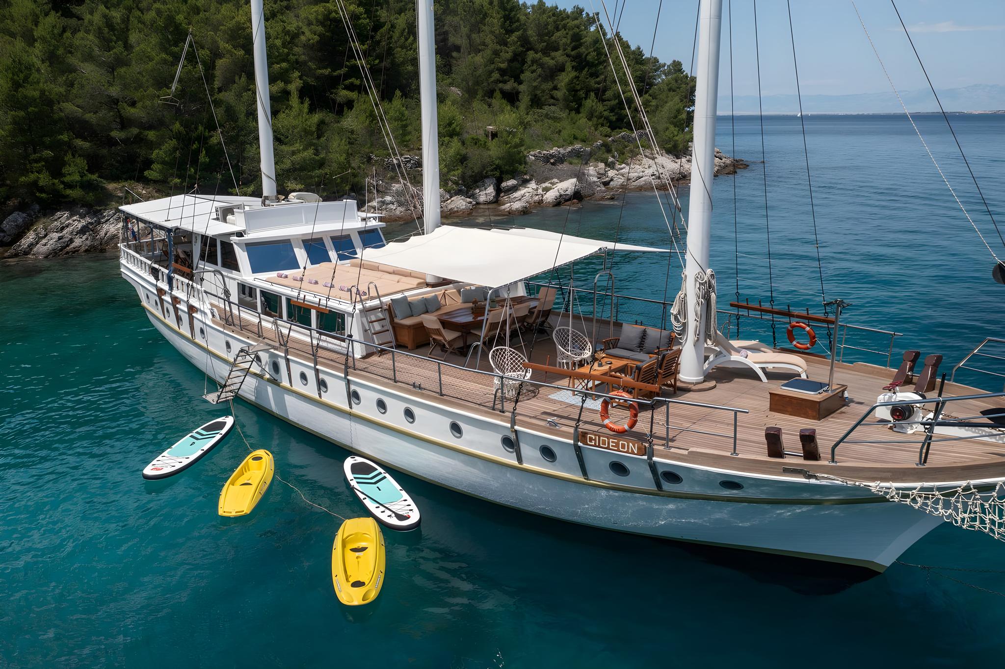 Traditional white gulet yacht Gideon anchored in turquoise waters with kayaks and paddleboards