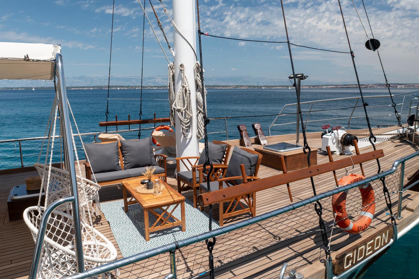 Gulet aft deck with teak dining chairs, coffee table and sailing rigging overlooking blue water