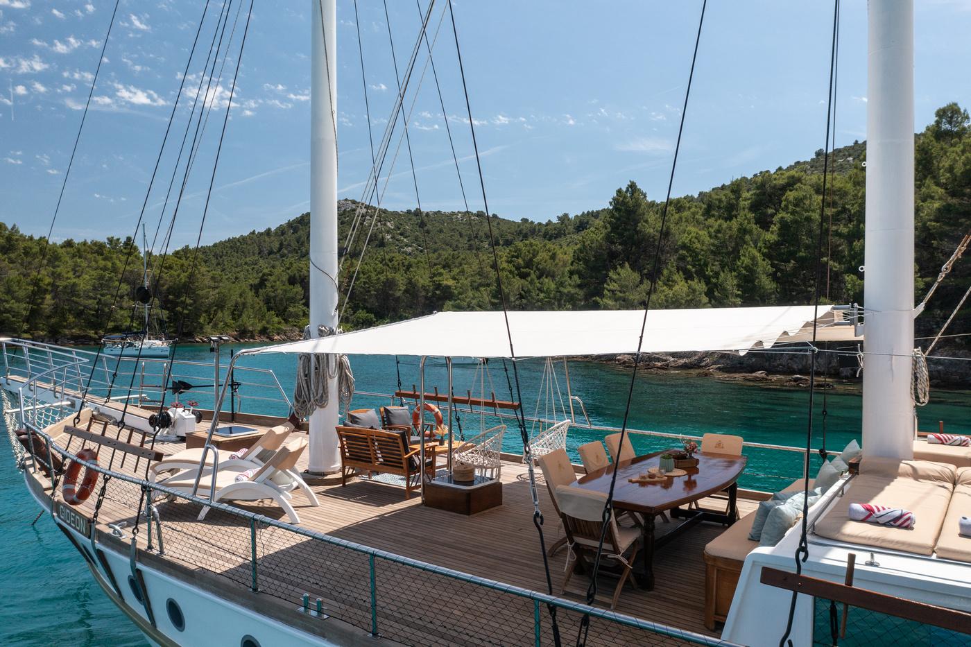 gulet main deck with round dining table, cushioned seating and white awning in turquoise bay