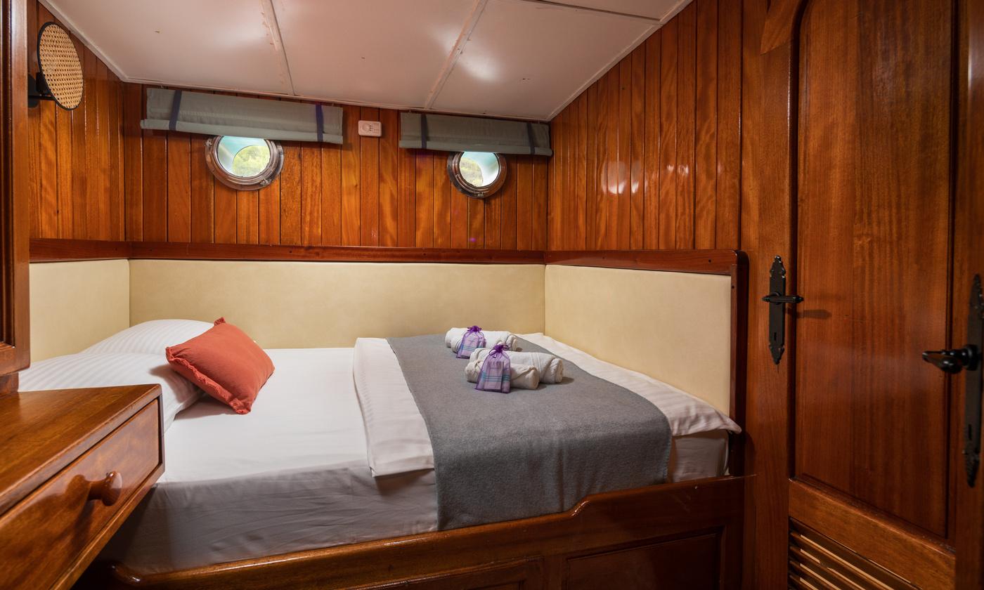 yacht guest cabin interior with double bed, cream upholstery, wooden paneling and twin portholes
