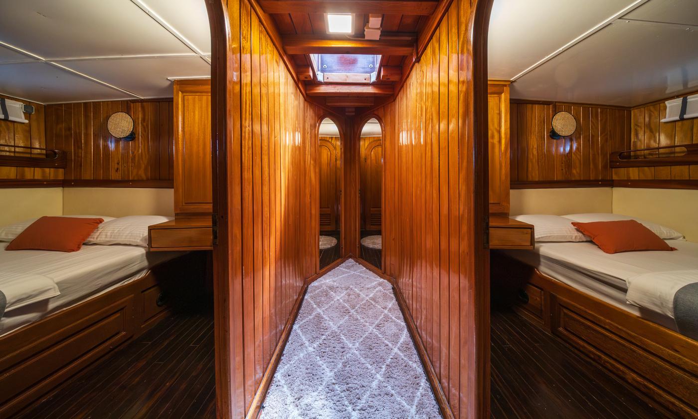 yacht guest cabin featuring twin beds with white linens and orange pillows separated by wooden walkway