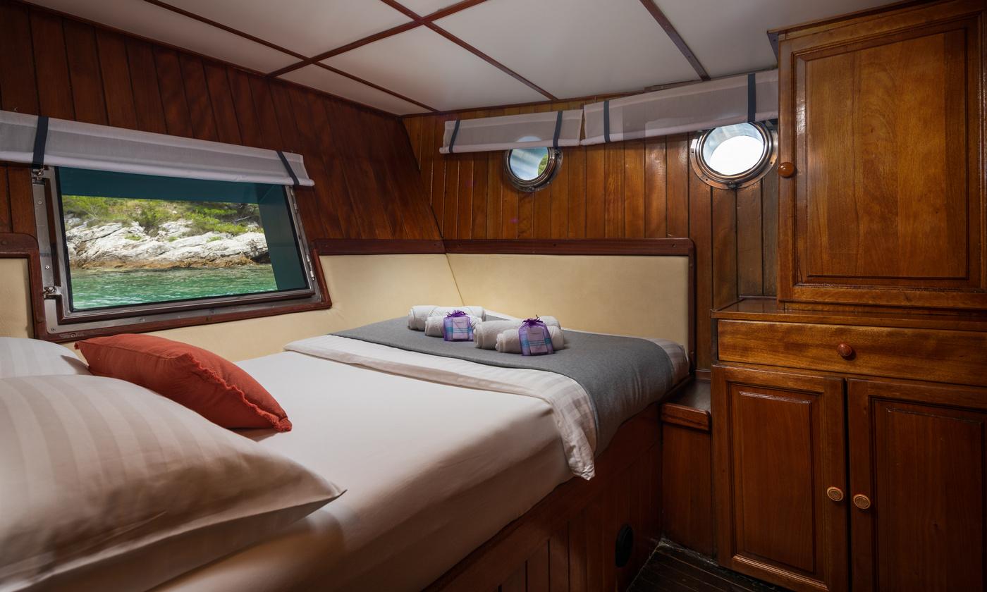 yacht guest cabin with double bed, cream headboard, wooden paneling and two portholes