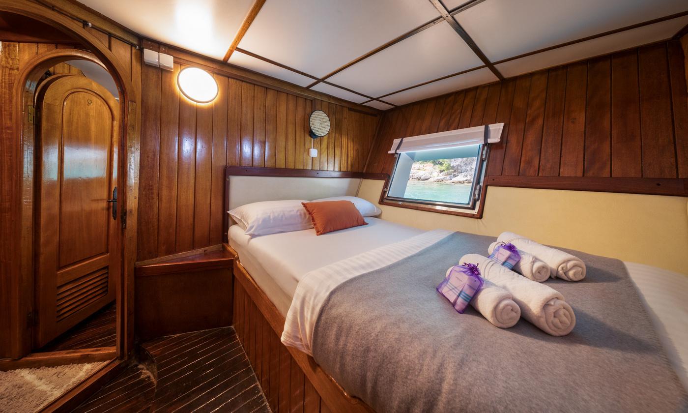 yacht guest cabin featuring double bed with white linens, rolled towels, wooden paneling and porthole window