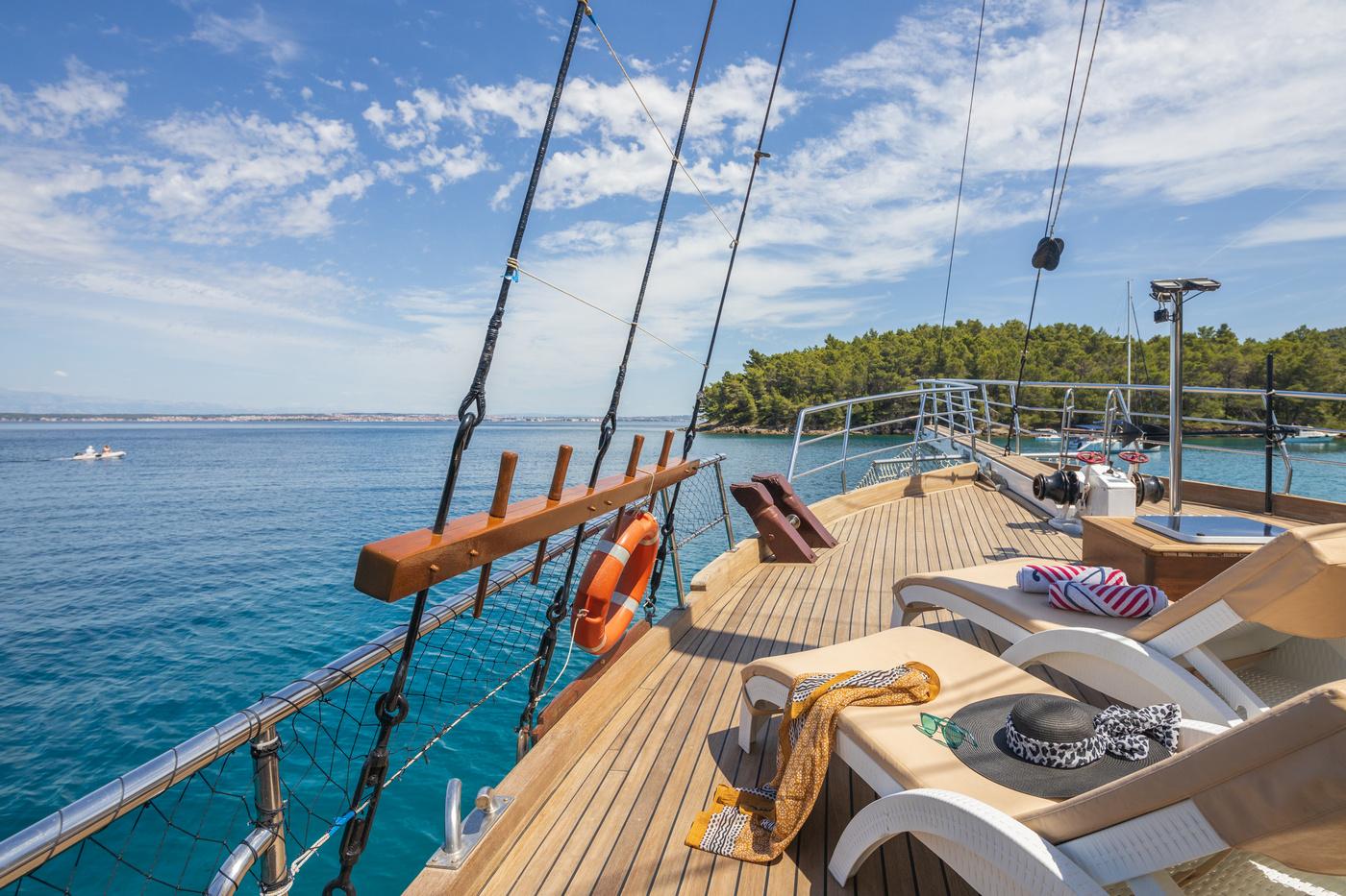 gulet sun deck with white loungers, teak decking, and sailing mast rigging overlooking blue waters