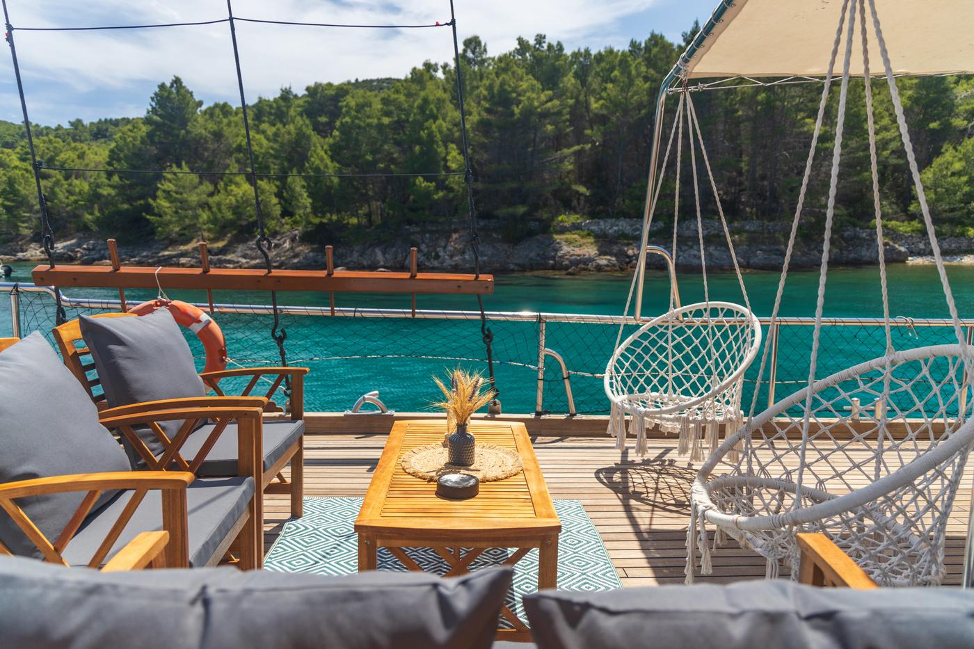 gulet aft deck with teak furniture, hanging wicker chairs and turquoise bay view