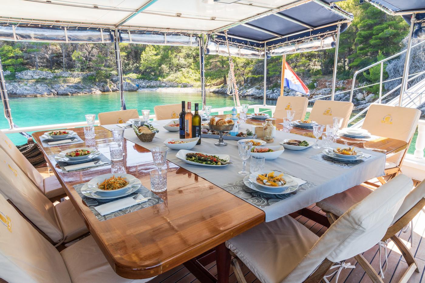 yacht aft deck dining table set with Mediterranean dishes and wine bottles overlooking turquoise bay