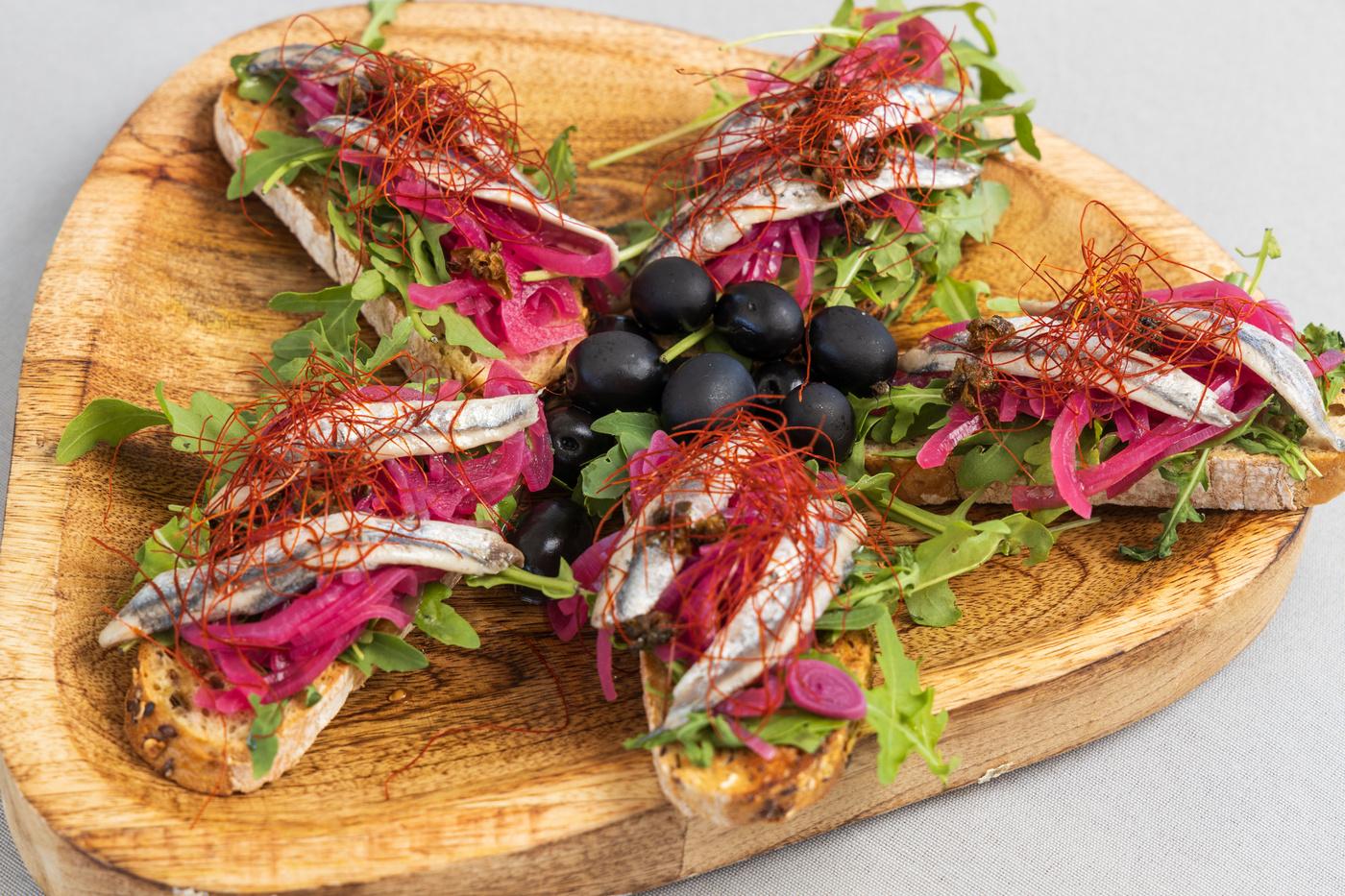 elegant anchovy canapes with pickled onions and black olives on wooden board