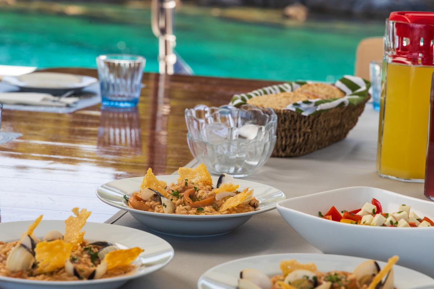Mediterranean dishes served on white plates at yacht dining table with turquoise water backdrop