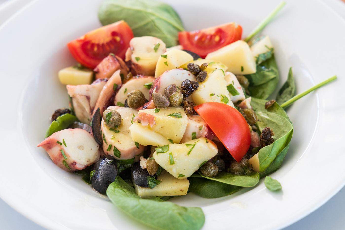 Fresh Mediterranean salad with black olives, capers, cherry tomatoes and mixed greens on white plate