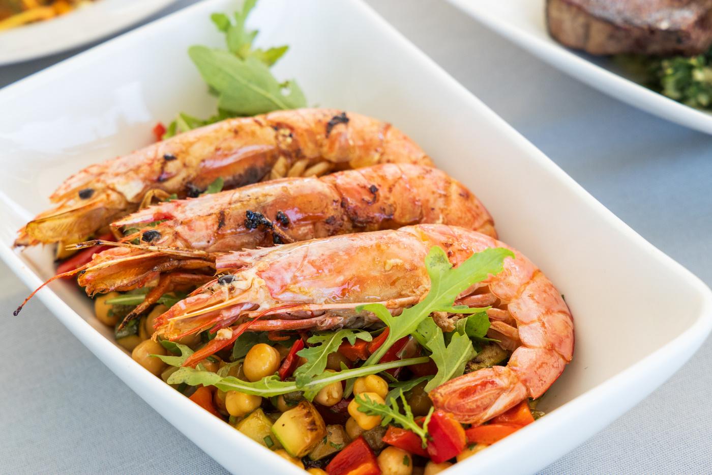 grilled prawns with arugula salad and vegetables served on white square plate