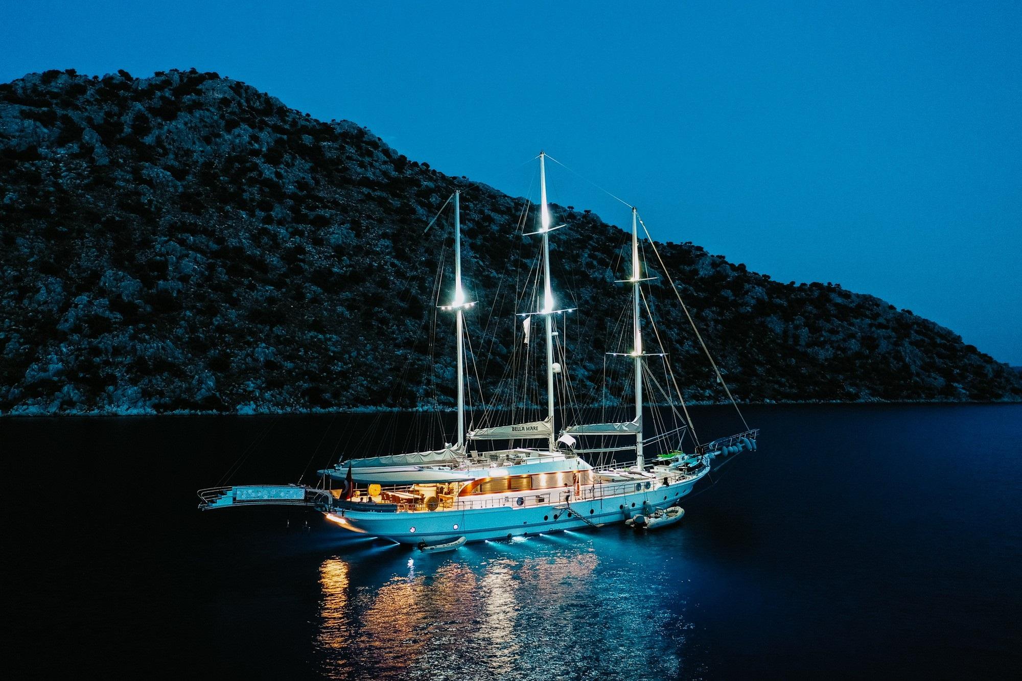 Traditional wooden gulet yacht anchored in calm bay at night with warm deck lighting