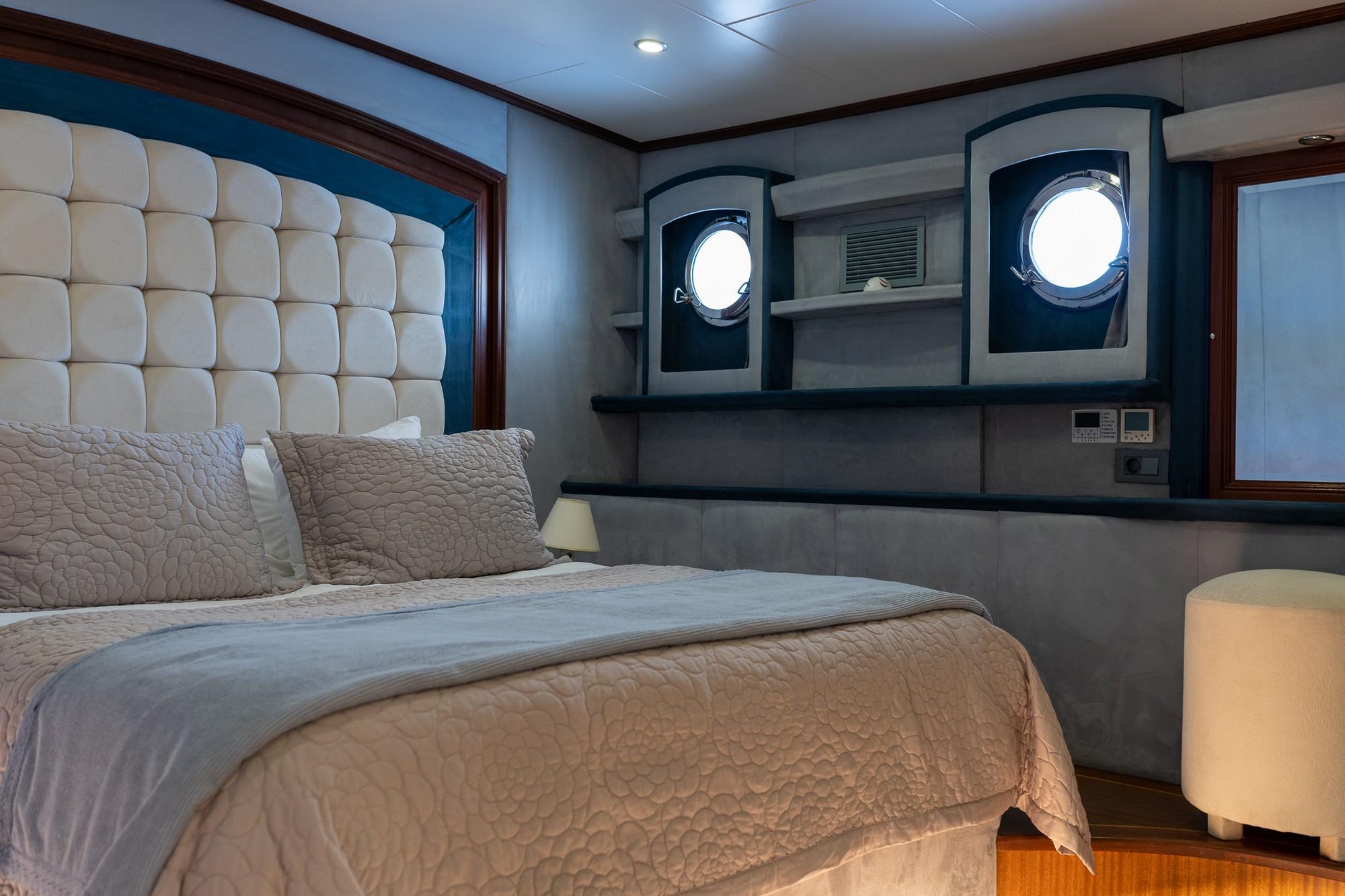 yacht cabin interior with cream quilted headboard, beige bedding, built-in storage and circular portholes