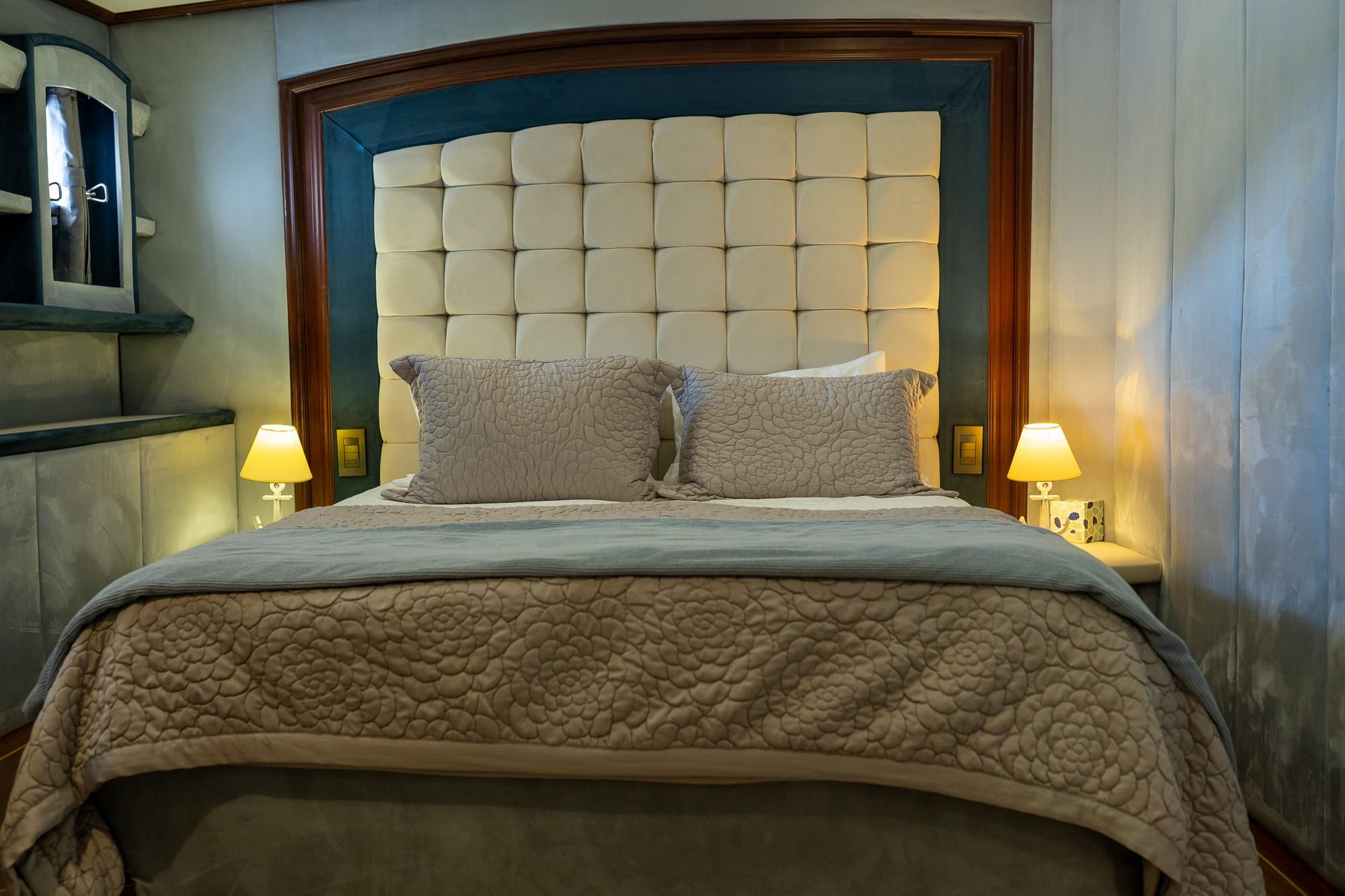 yacht cabin interior featuring cream tufted headboard, quilted bedding and built-in nightstand lighting