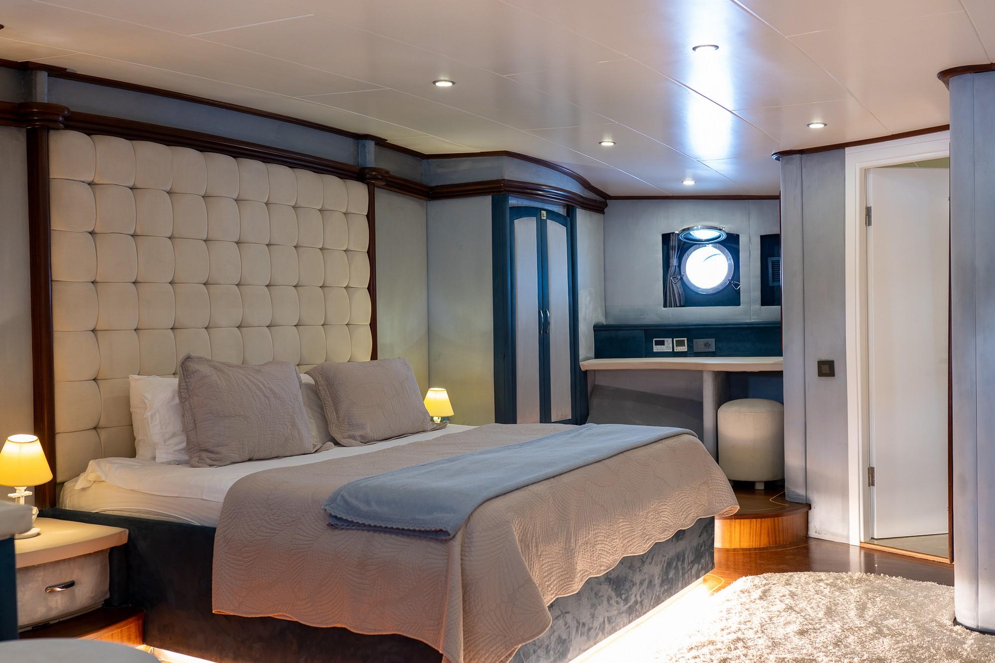 yacht cabin interior with cream tufted headboard, double bed and circular porthole window