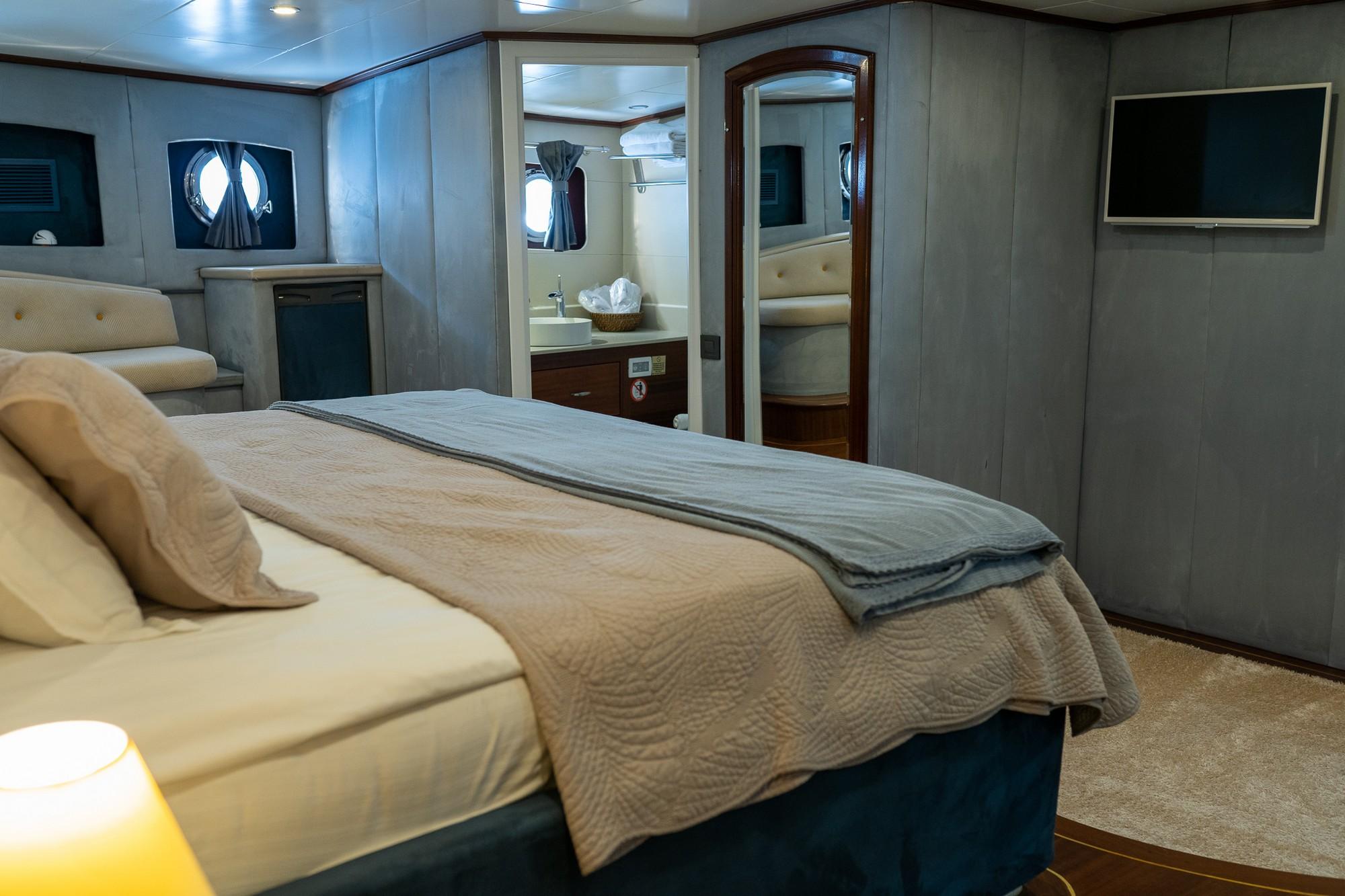 yacht cabin interior with beige quilted bedding and ensuite bathroom visible through doorway