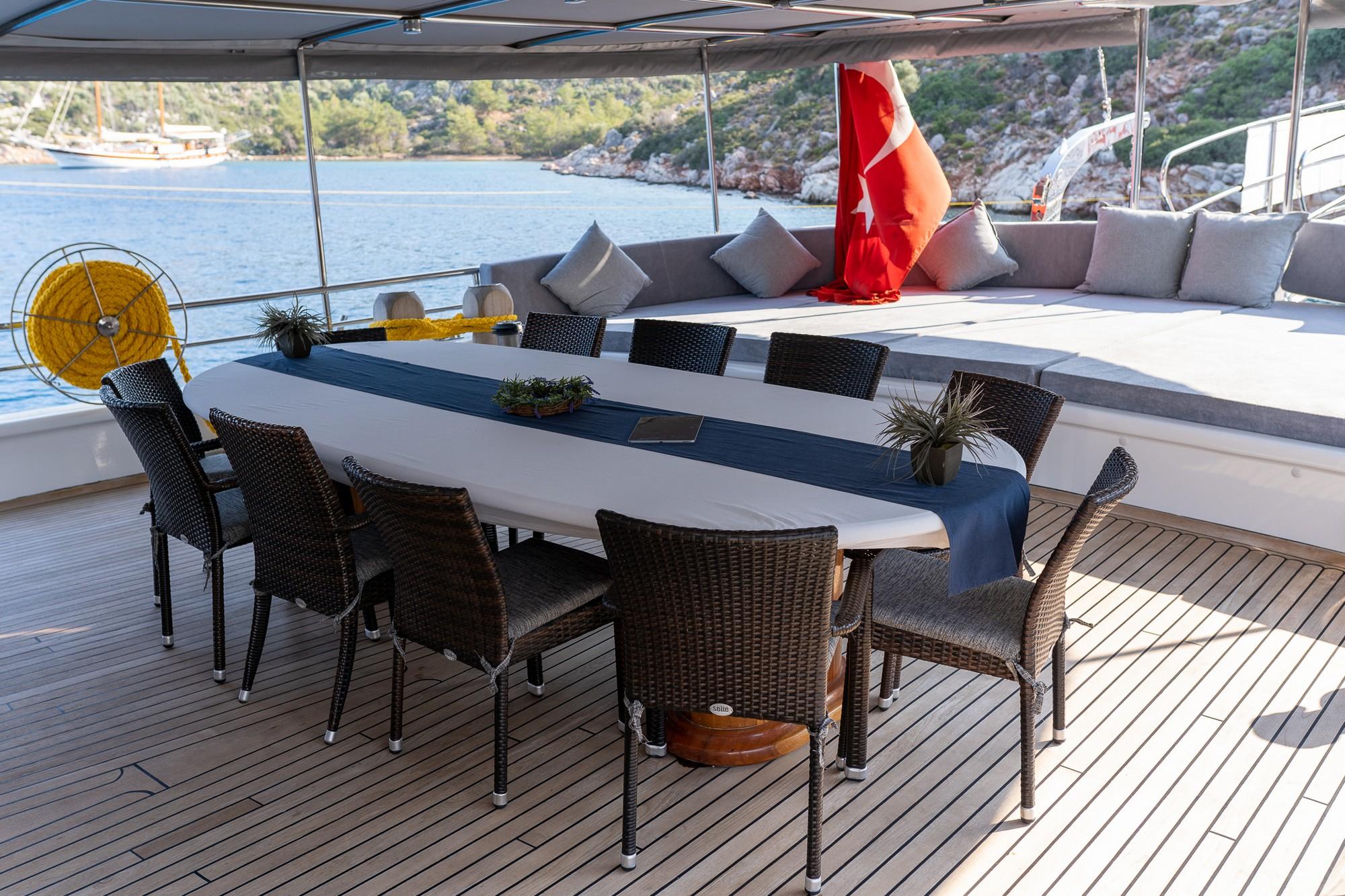 yacht aft deck with white dining table, wicker chairs and cushioned seating area