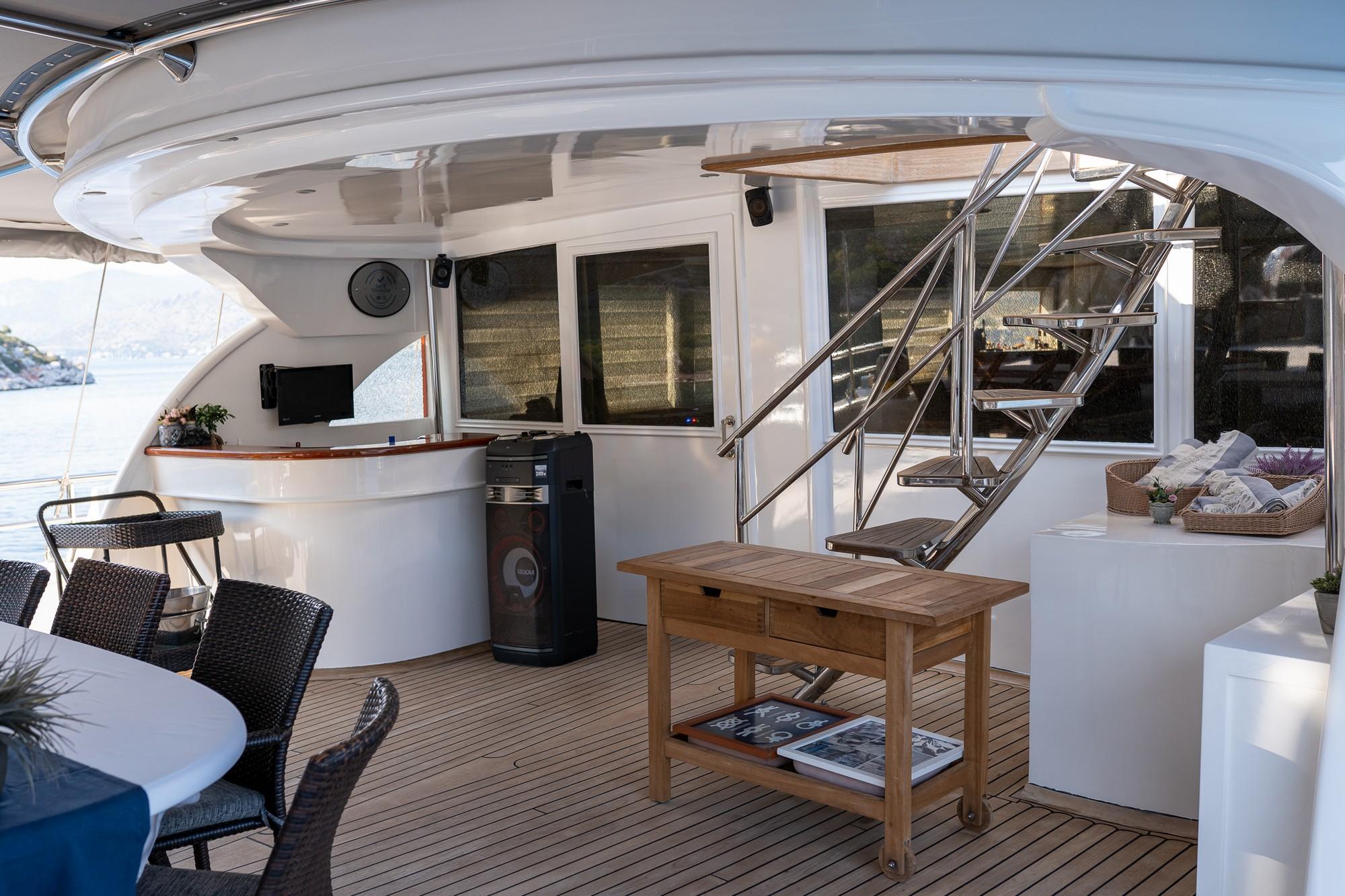 yacht aft deck with curved white seating, wooden coffee table, and stainless steel stairs to upper deck