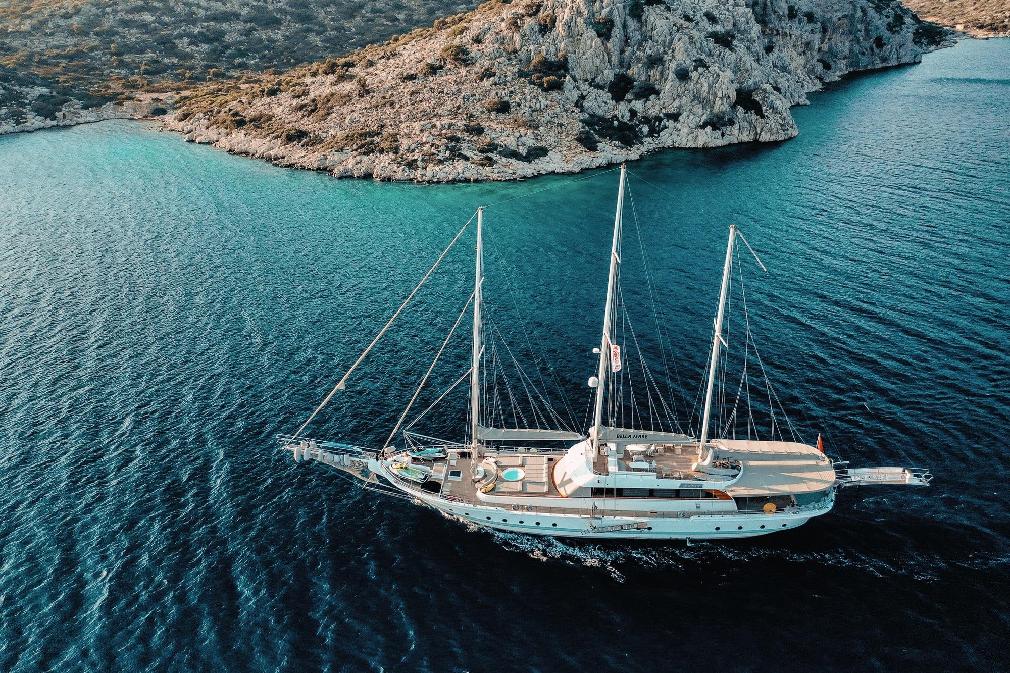 aerial view of white three-masted gulet anchored in crystal clear turquoise Mediterranean bay
