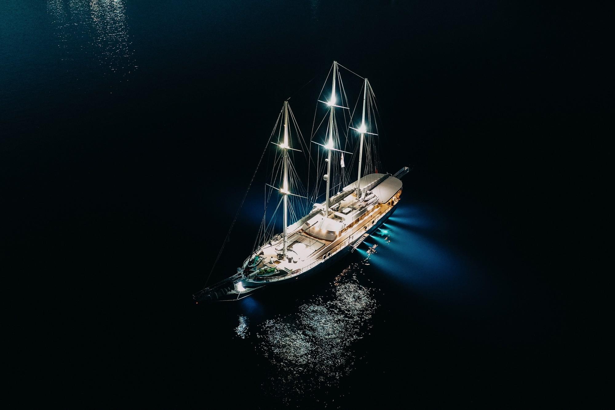 aerial night view of illuminated three-masted sailing yacht anchored in dark waters