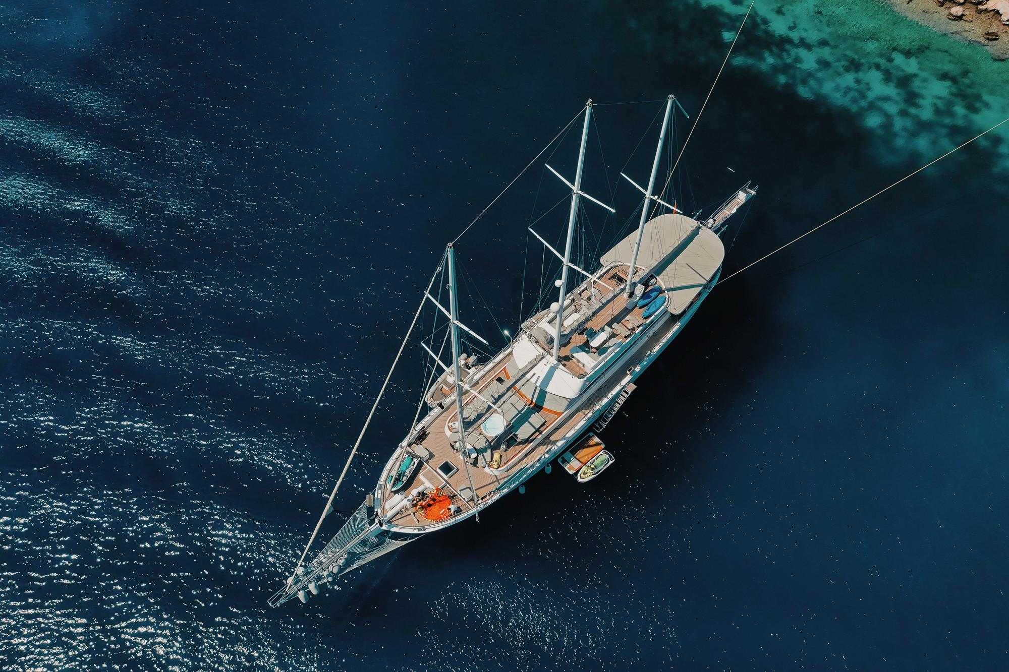 aerial view of traditional sailing yacht with multiple masts anchored in crystal clear turquoise waters