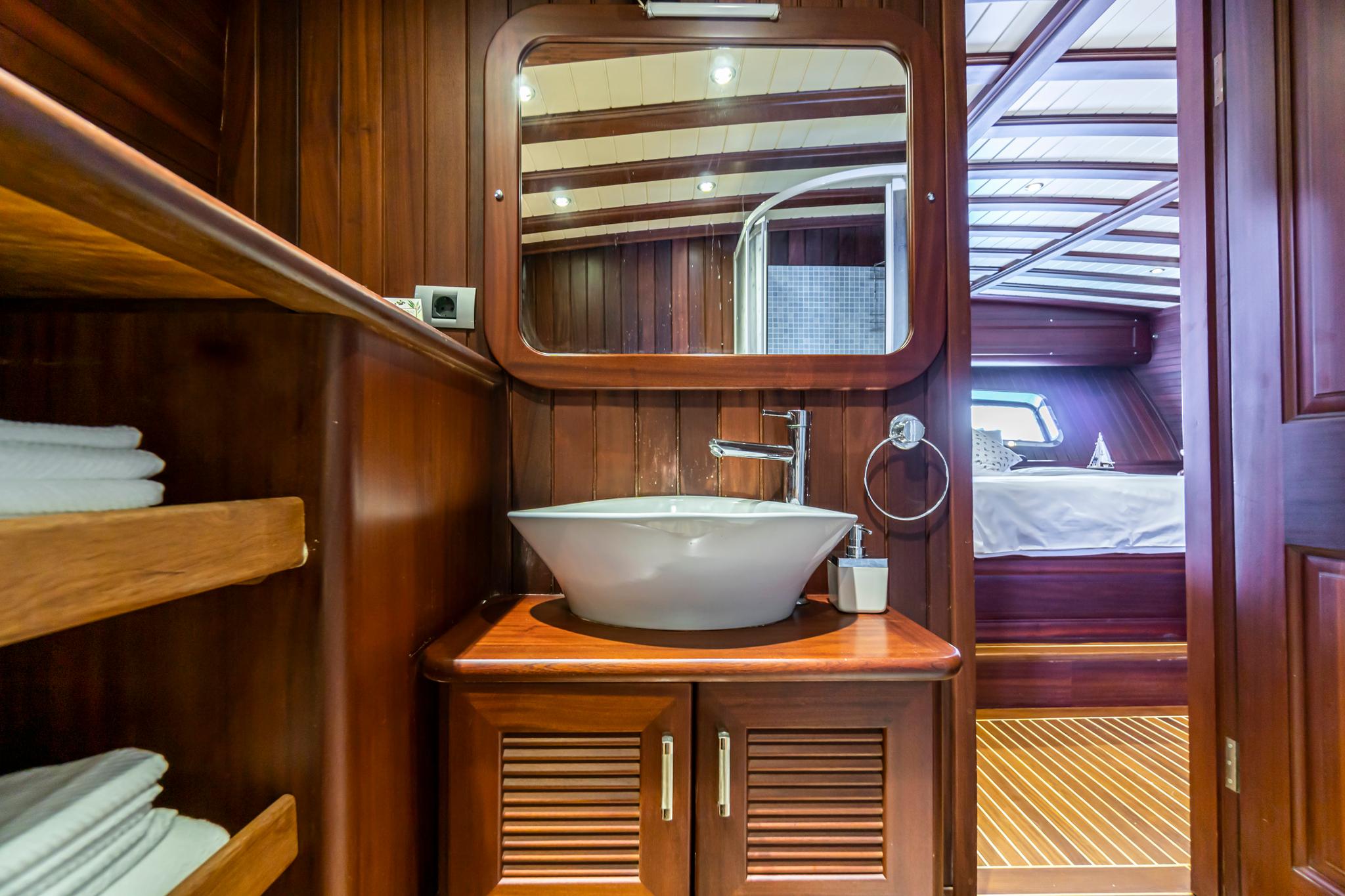 yacht bathroom featuring white vessel basin on wooden vanity with rounded mirror