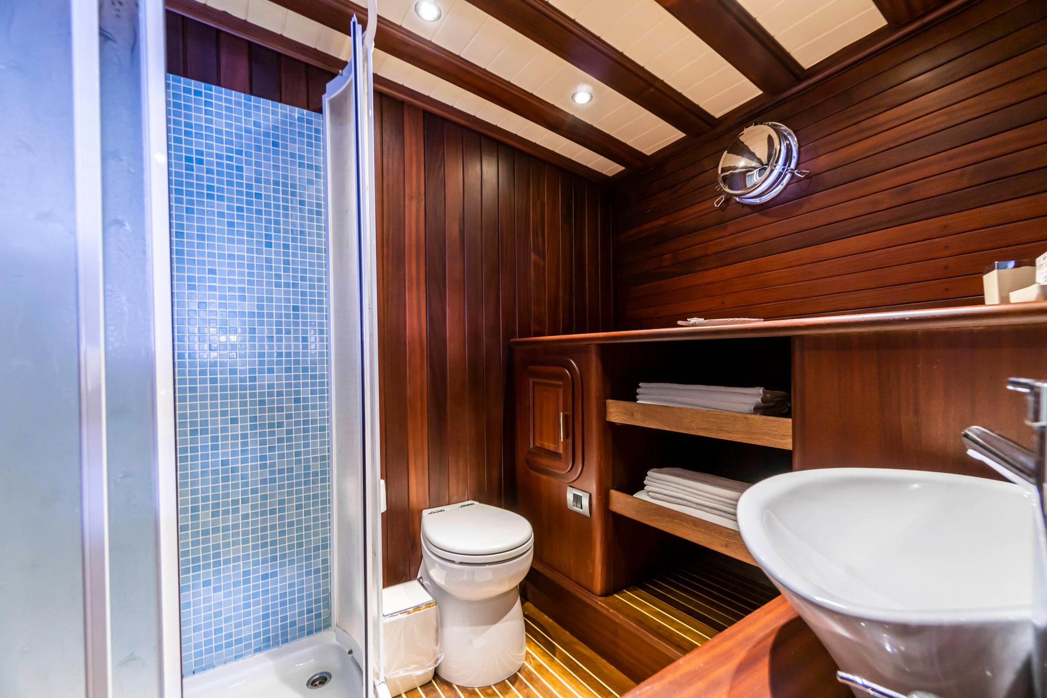 yacht bathroom interior with blue mosaic shower, toilet and wooden storage shelving