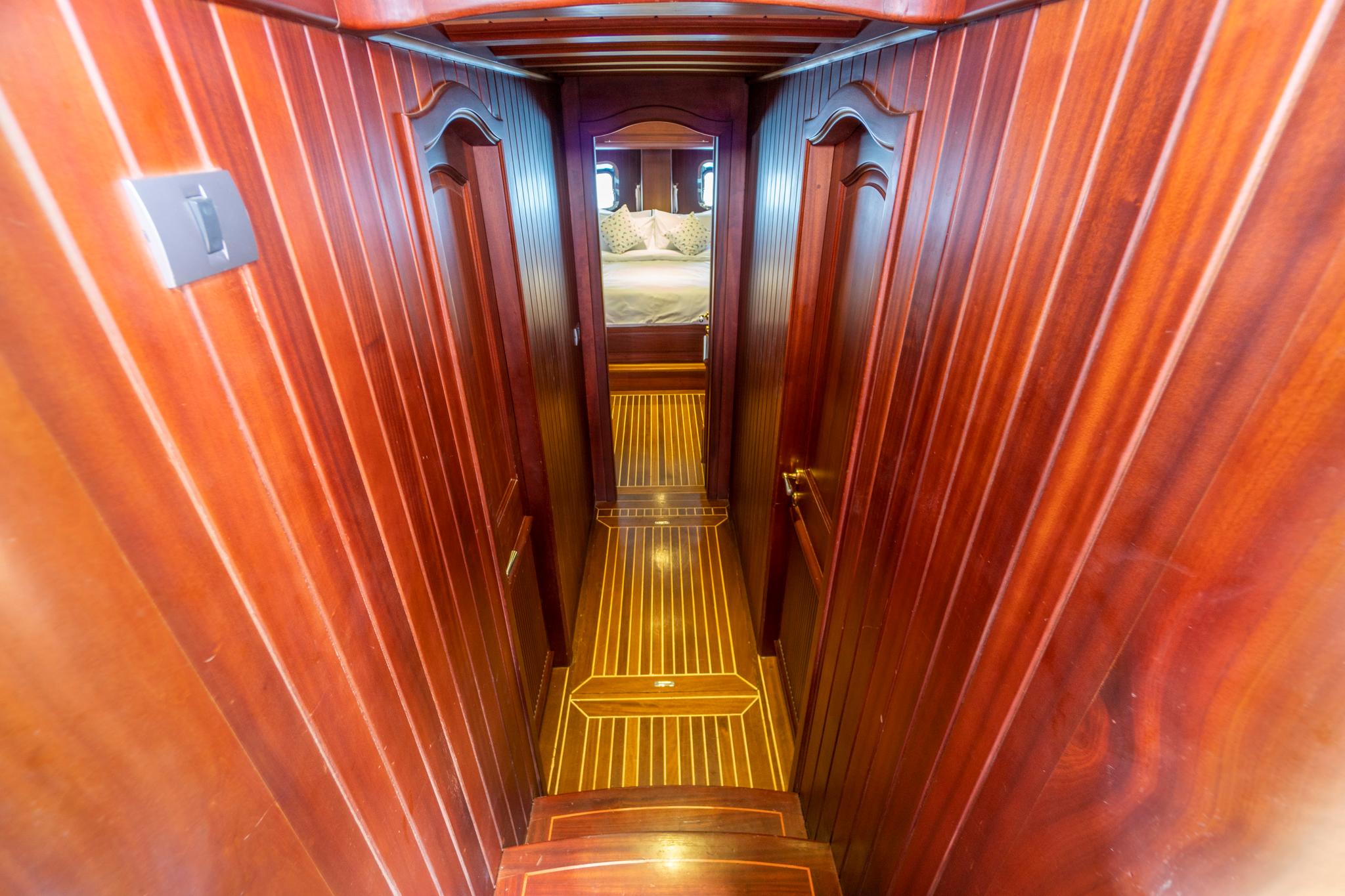 yacht interior corridor with polished wood paneling and steps leading to cabin with bed visible