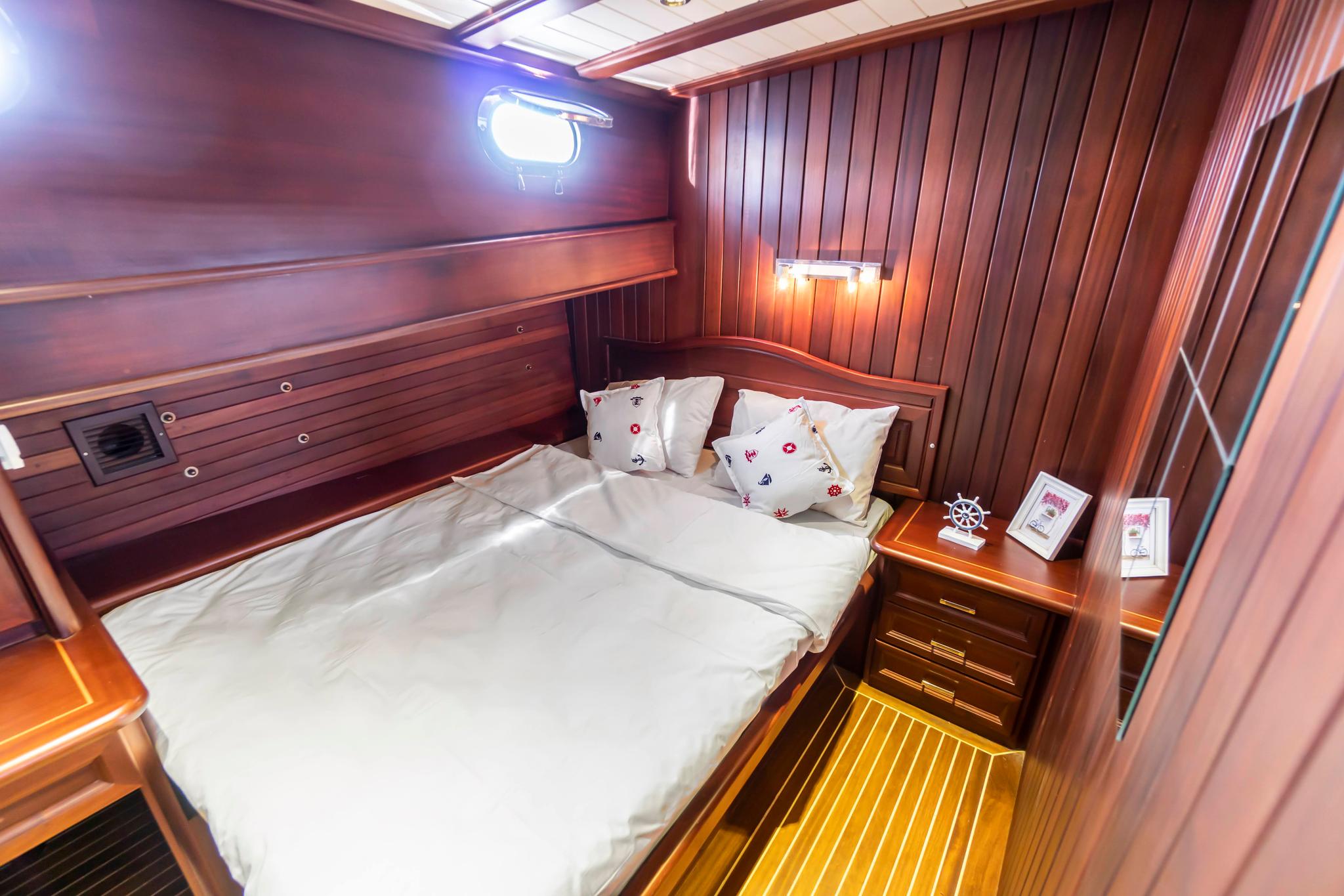 yacht guest cabin featuring double bed with white linens and nautical pillows in rich wood interior