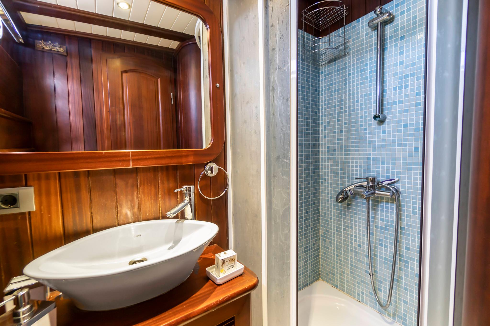 yacht bathroom featuring white oval vessel sink on teak vanity and blue mosaic tiled shower stall