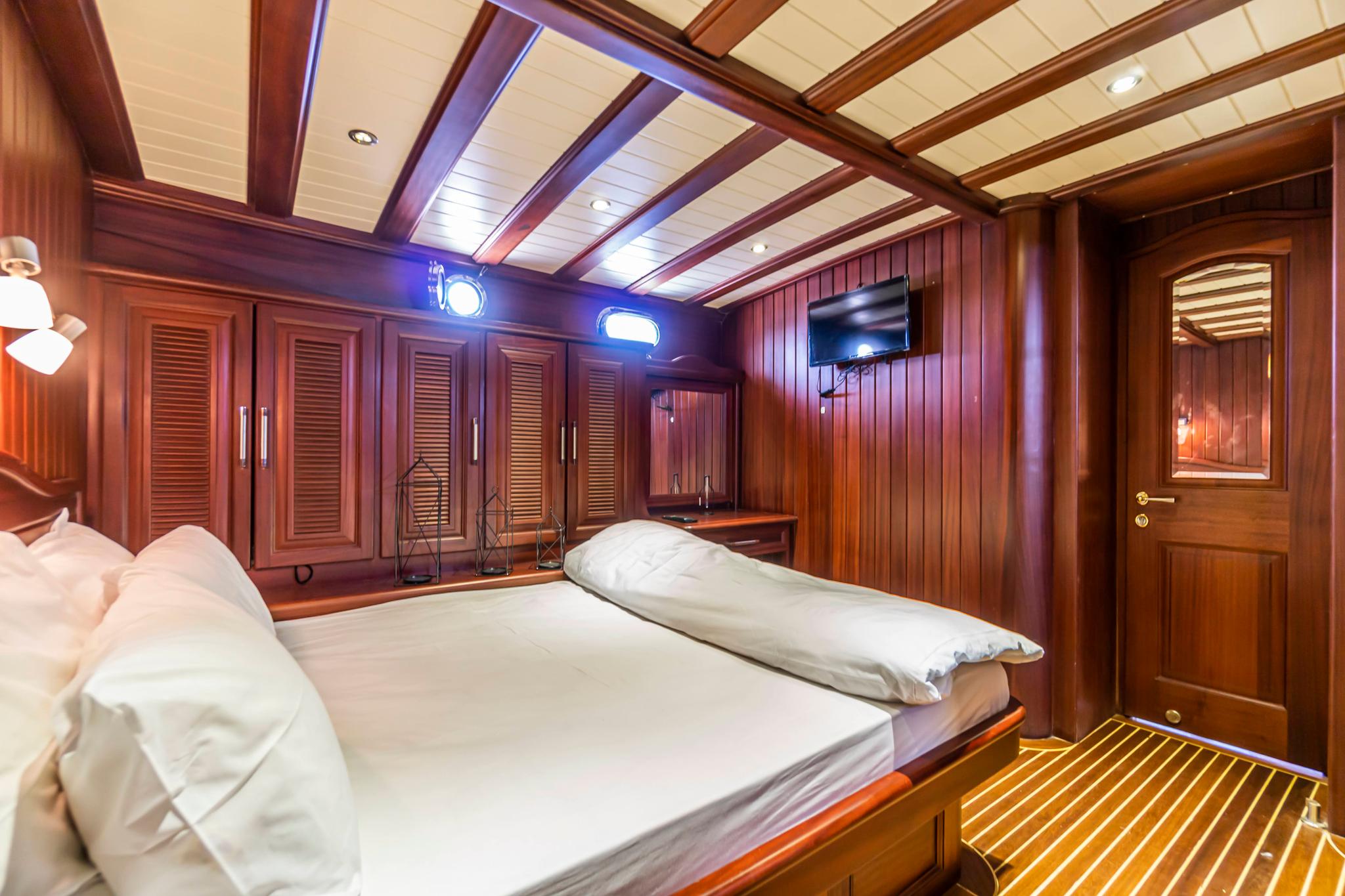 yacht guest cabin featuring double bed with white linens and rich mahogany wood paneling