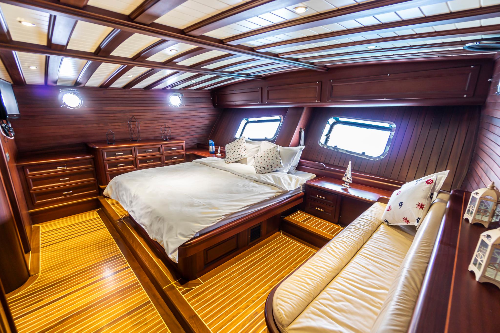 yacht cabin interior with double bed, built-in storage, teak flooring and cream upholstered sofa
