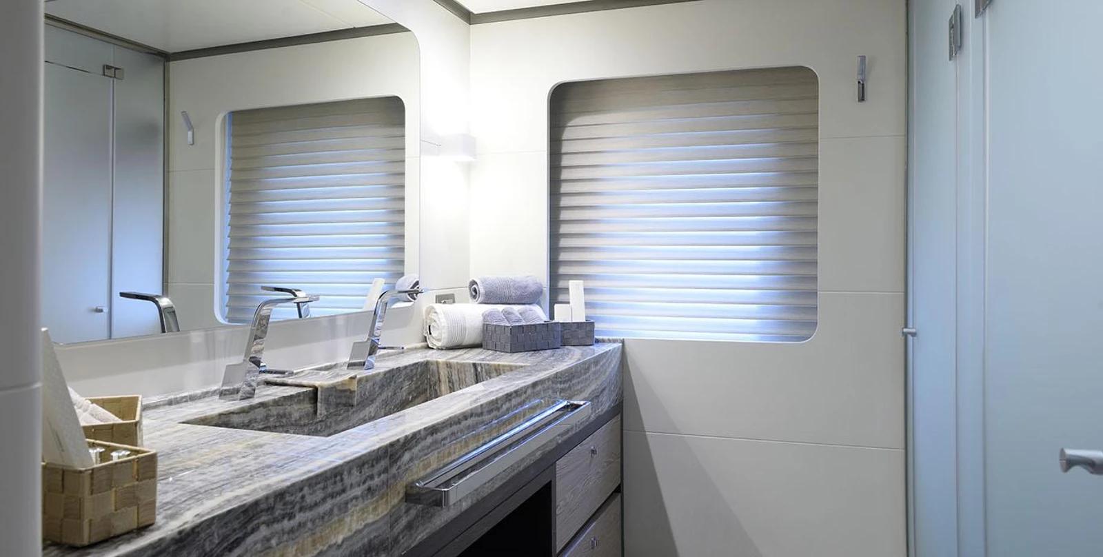 modern yacht bathroom featuring marble countertop vanity, chrome fixtures, and two rectangular portholes with blinds