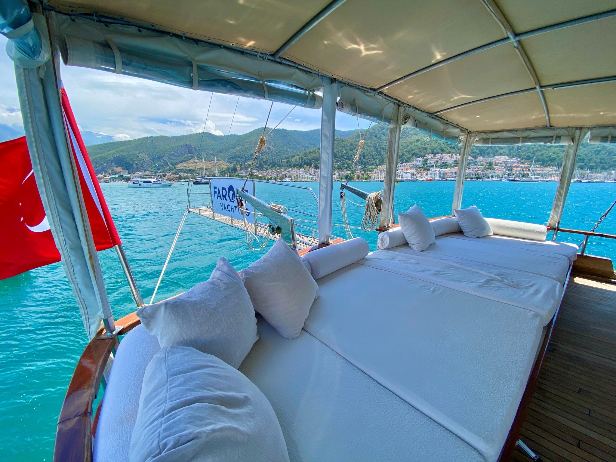 Covered aft deck lounge with white cushioned seating and panoramic windows overlooking turquoise bay