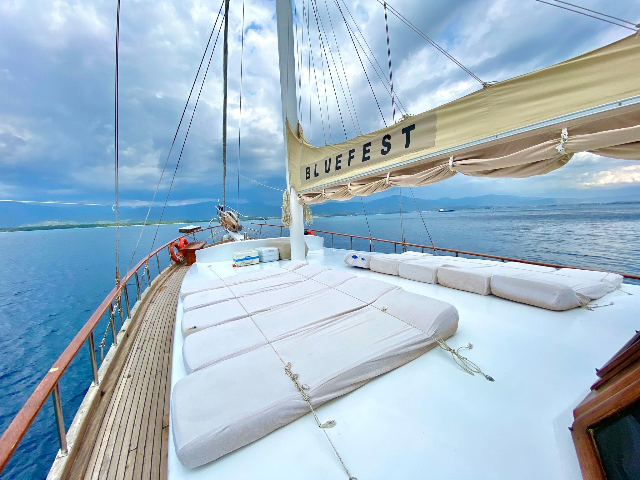 Gulet bow sun deck with white cushioned loungers under cream sail at sea