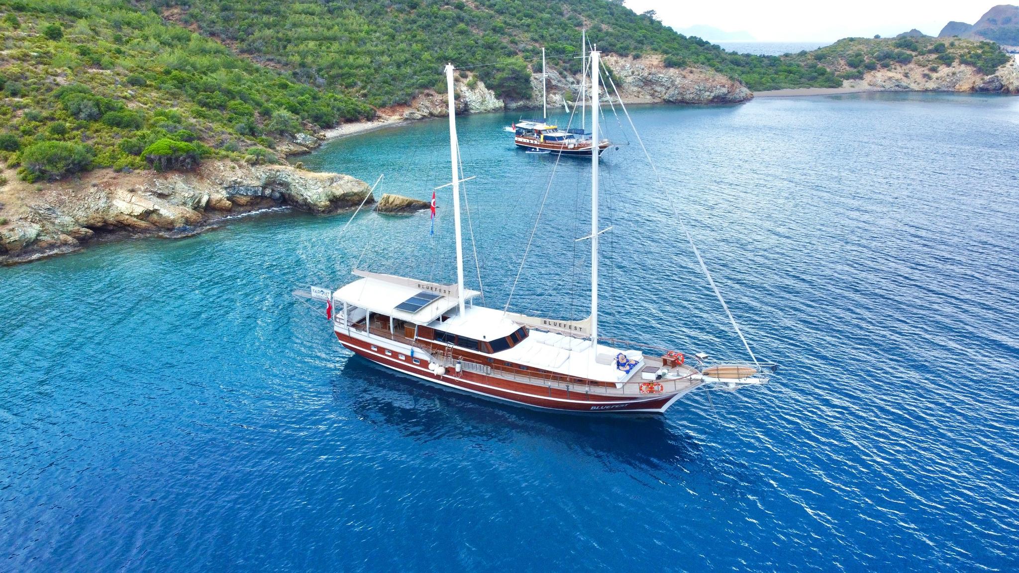 aerial view of traditional wooden gulet yacht anchored in turquoise Mediterranean bay with rocky coastline